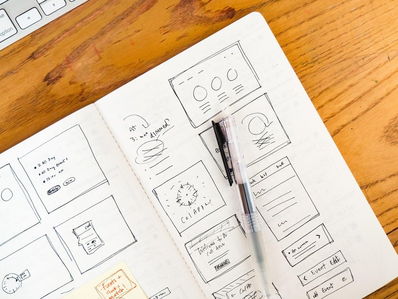Hand-drawn app wireframes in a notebook on a wooden desk